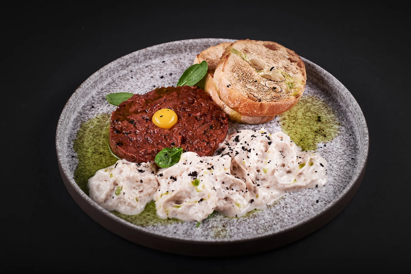 Restaurant plate with tartare and garnish on dark stone
