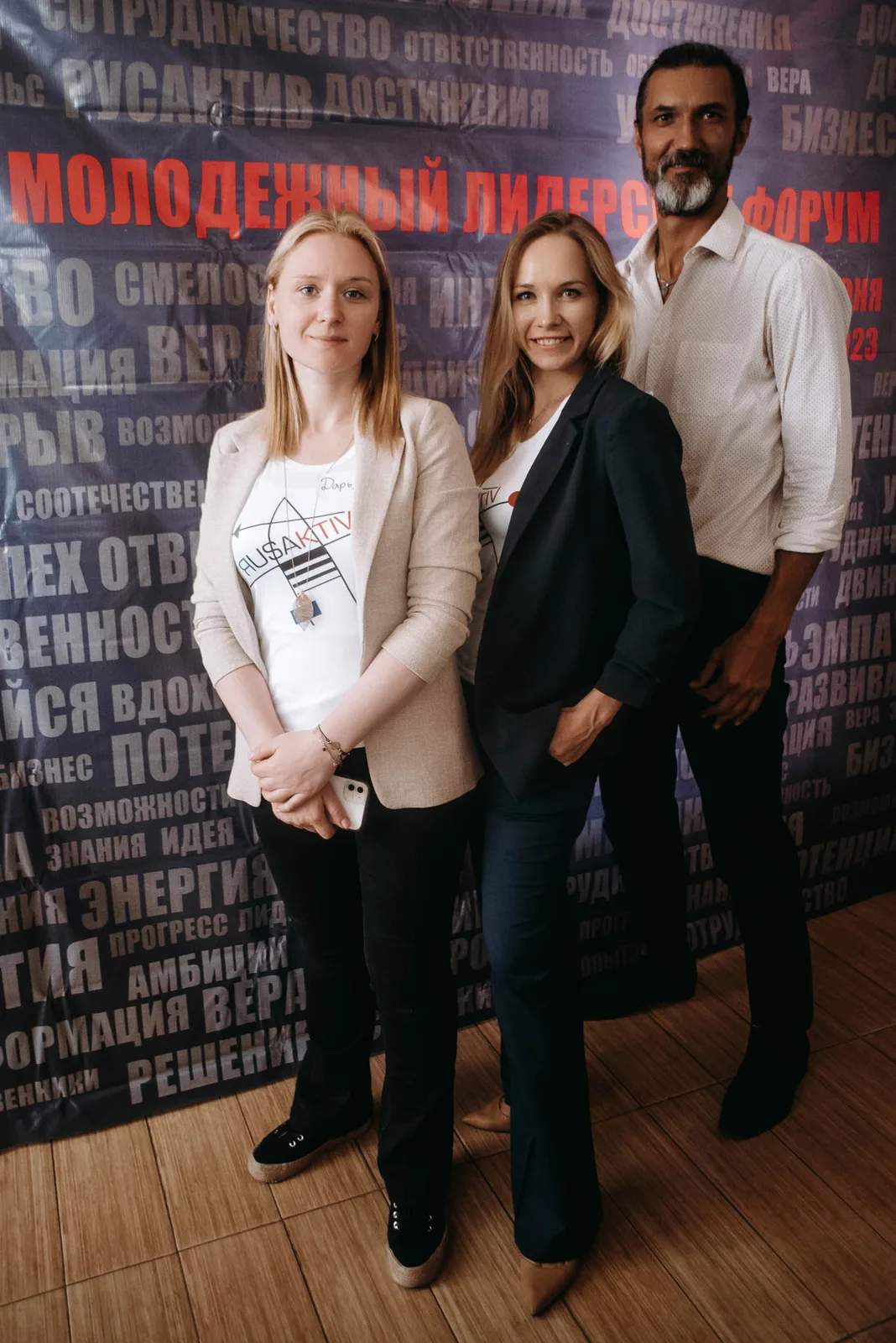 Three attendees posing at the press wall of a forum