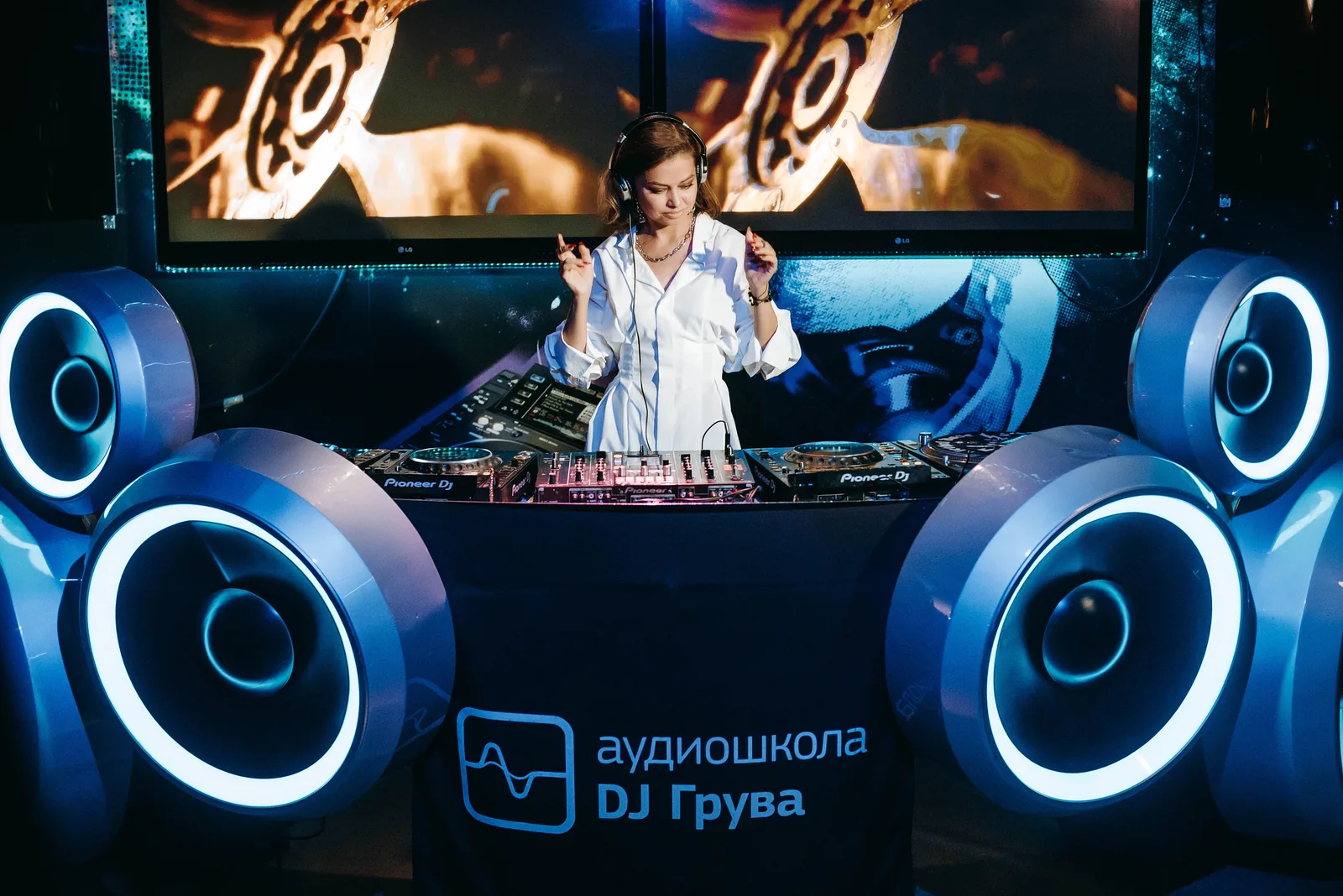 DJ performing in a booth flanked by big speakers at a school showcase