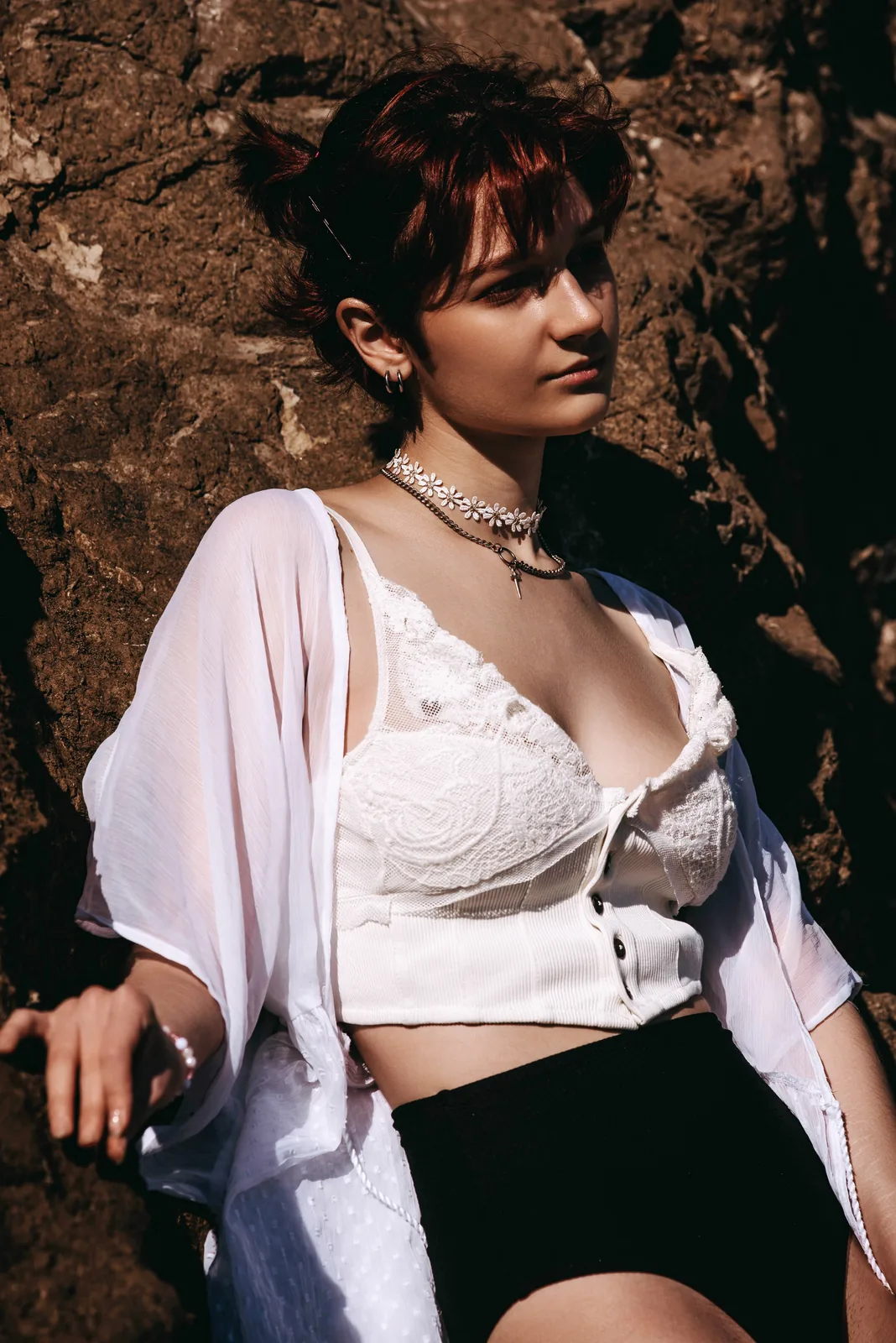 Model in an open white shirt posing on dark coastal rocks above the ocean, 2023