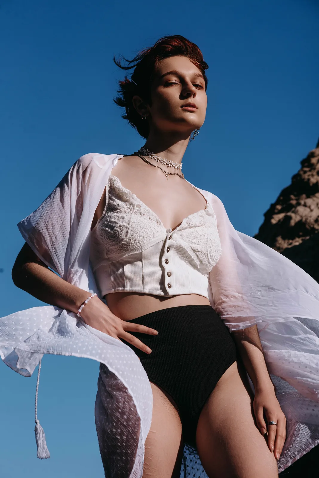 Low-angle fashion portrait of a model in a white corset top against a deep blue sky