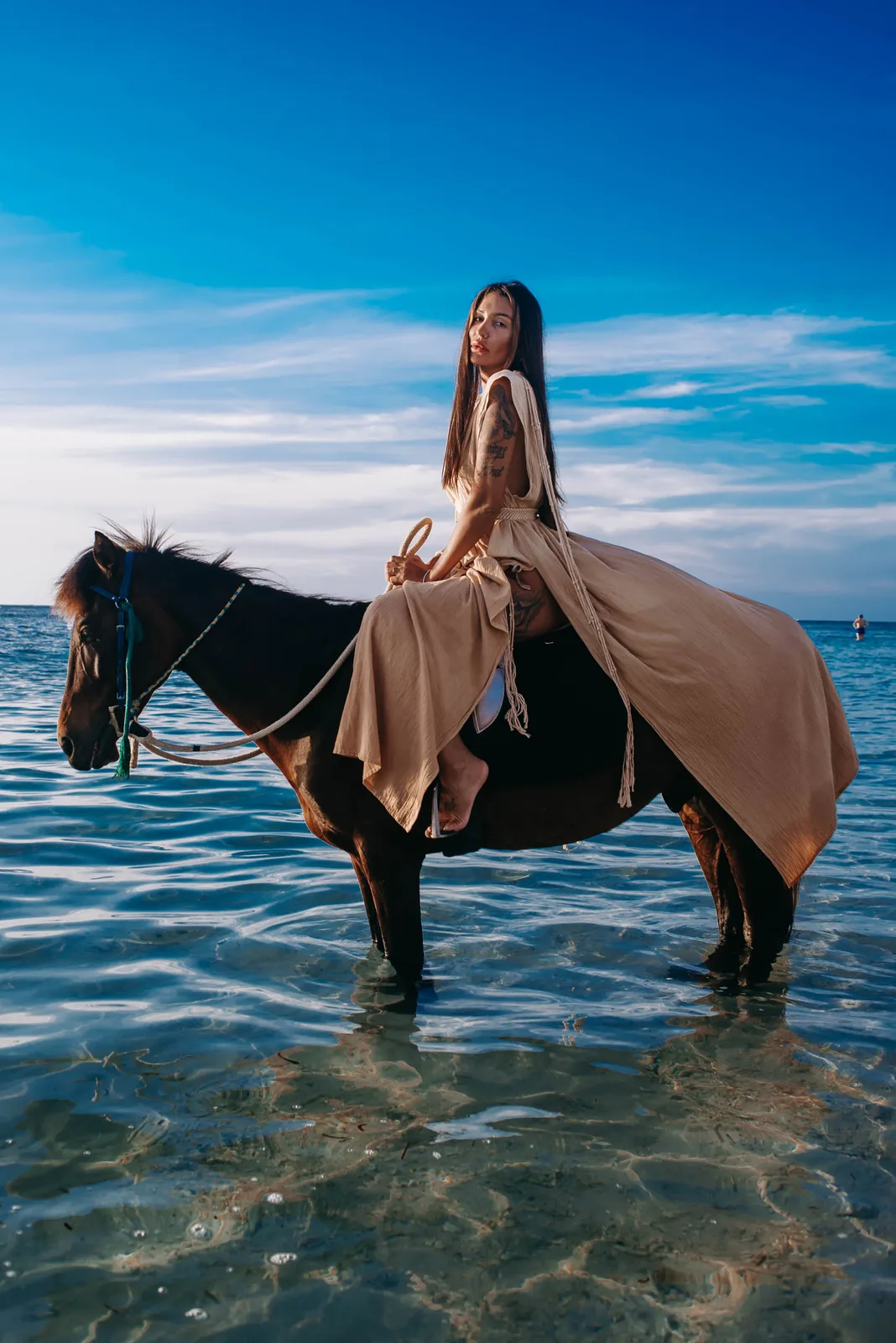 Rider in a long dress sitting on a horse standing in turquoise ocean water