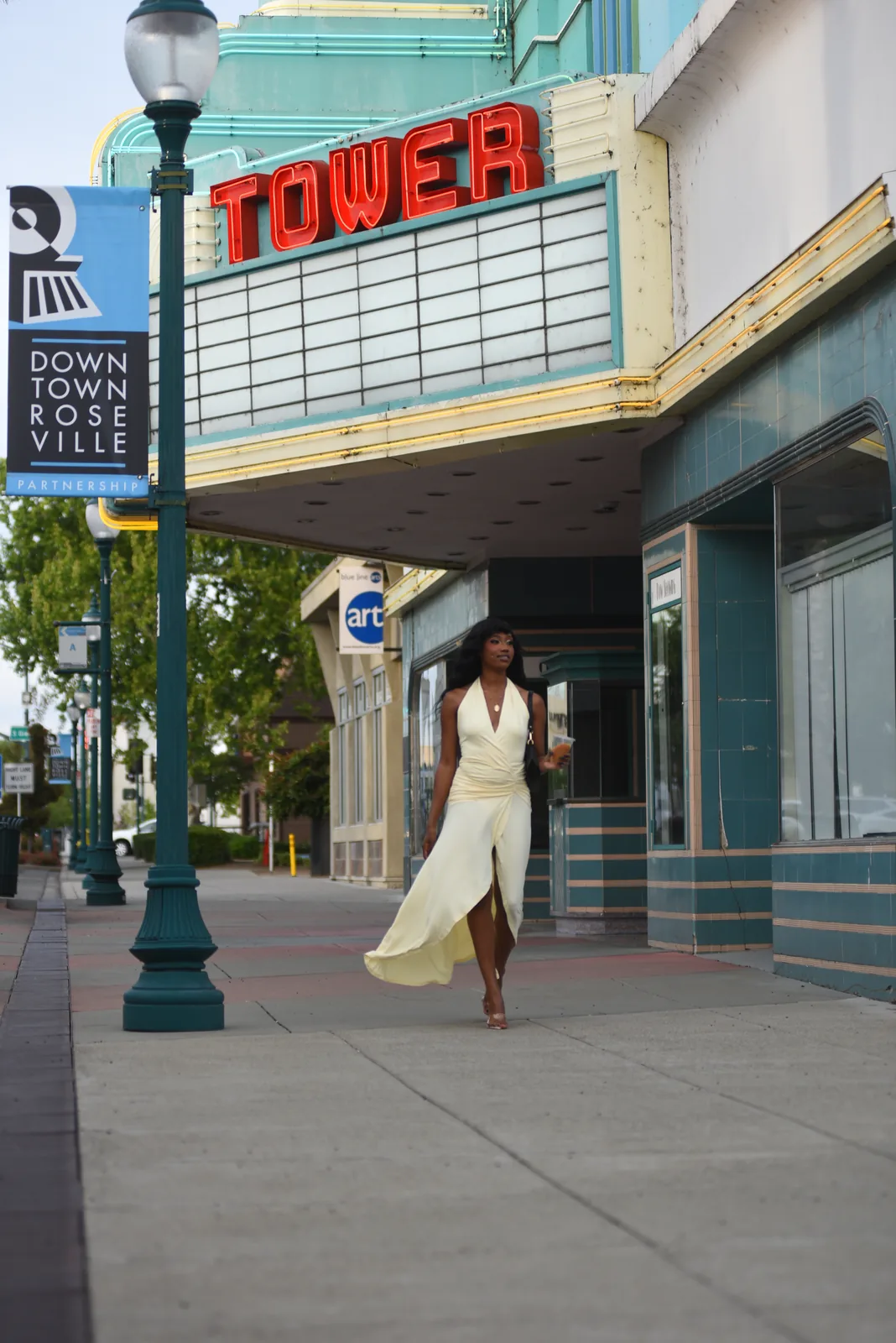 Model in a cream dress walking past the Tower Theatre marquee in Downtown Roseville, California