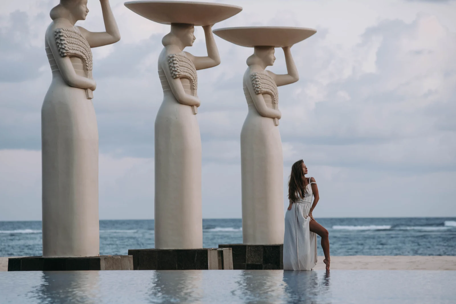 Woman in white by statues at an infinity pool