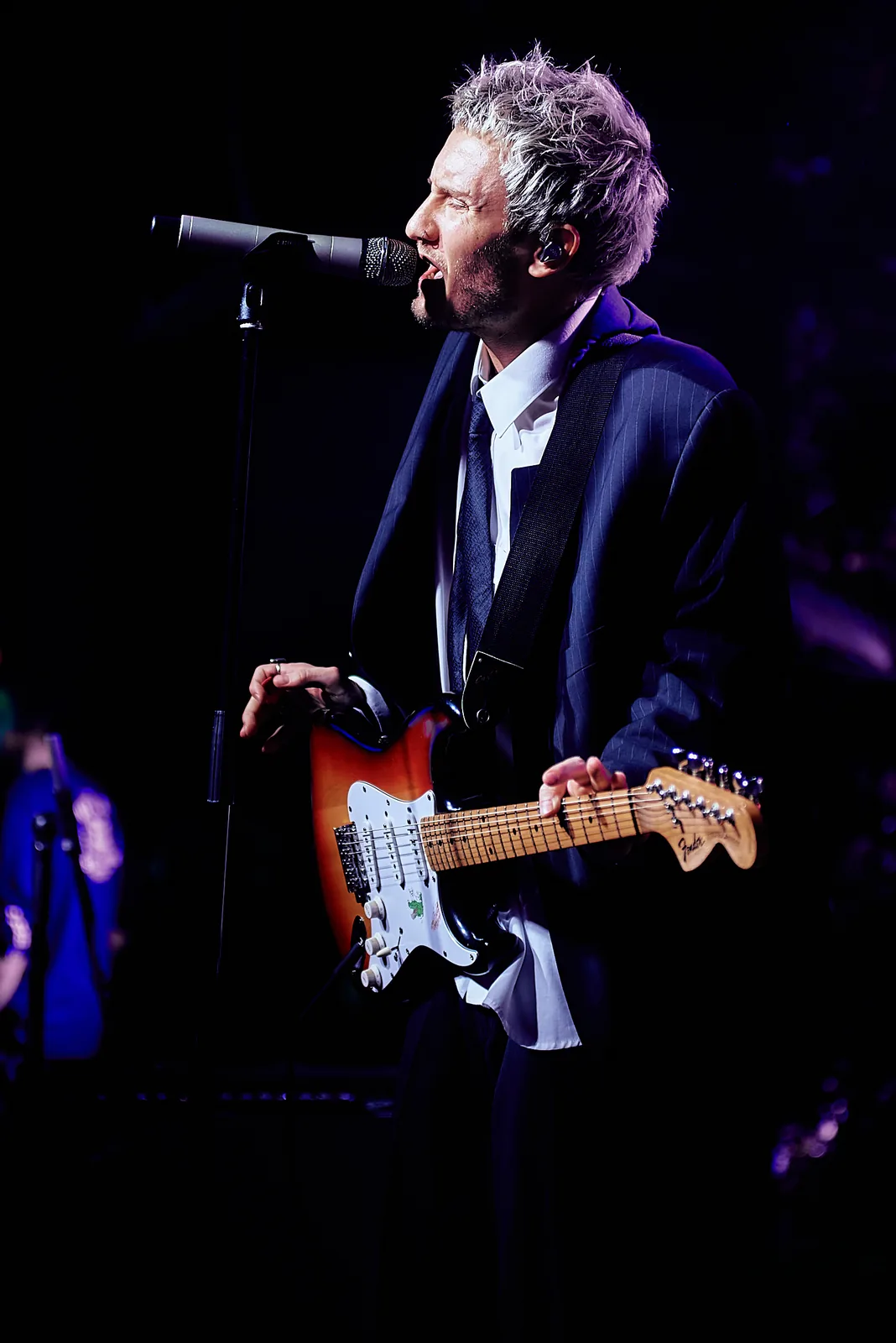 Grey-haired singer-guitarist performing under blue stage light