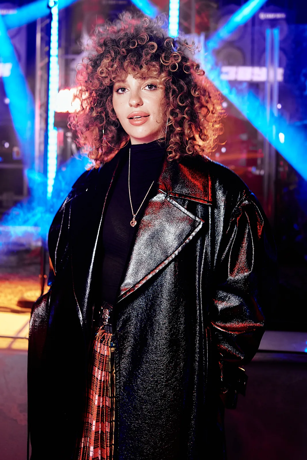 Curly-haired artist in a leather coat backstage, colourful backlight