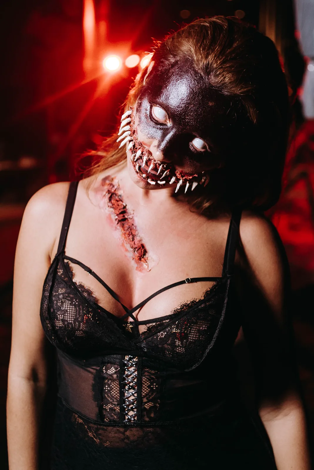 Guest in skull face paint and black lace at a Halloween party, red light