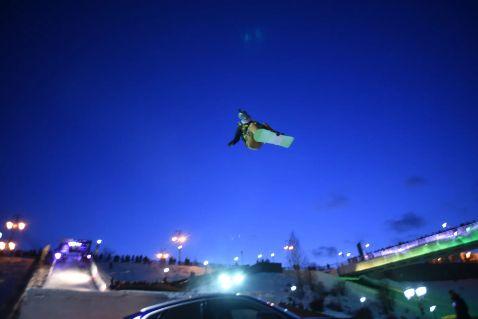 Night snowboard jump above the lit bridge