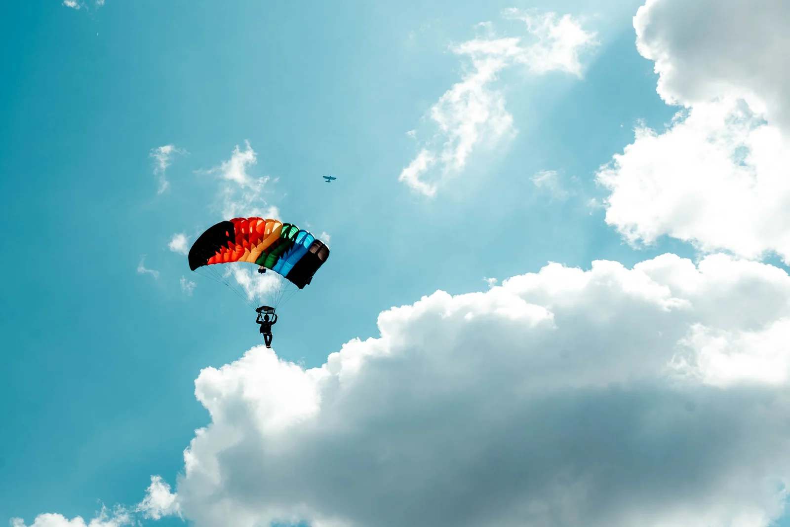 Skydiver with a rainbow canopy landing at a city festival